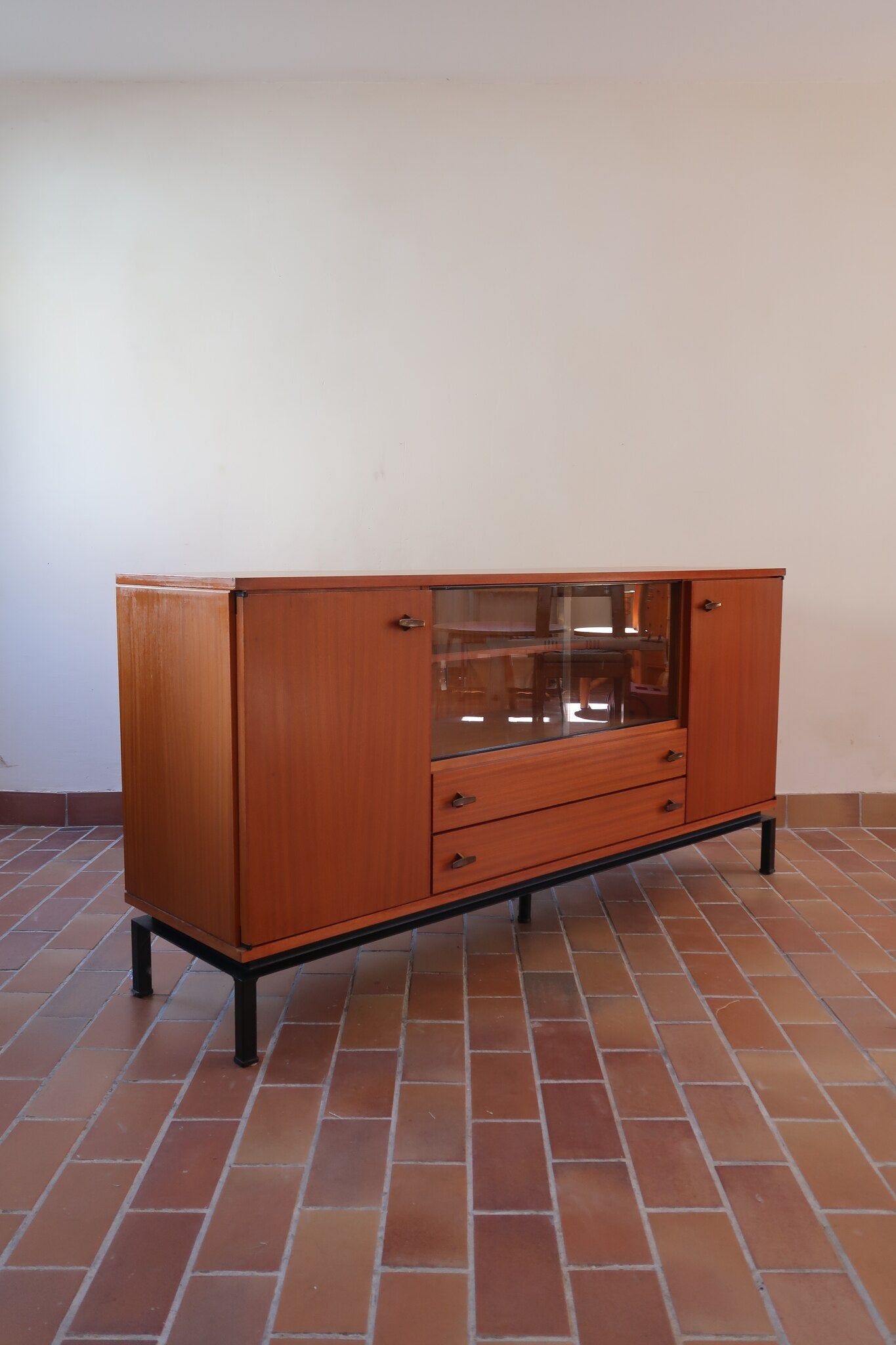 Enfilade vintage en teck années 60, deux portes pleines encadrant une vitrine centrale à portes coulissantes en verre, deux tiroirs, poignées navette métal, piétement métal laqué noir