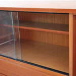 Enfilade vintage en teck années 60, deux portes pleines encadrant une vitrine centrale à portes coulissantes en verre, deux tiroirs, poignées navette métal, piétement métal laqué noir