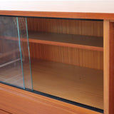 Enfilade vintage en teck années 60, deux portes pleines encadrant une vitrine centrale à portes coulissantes en verre, deux tiroirs, poignées navette métal, piétement métal laqué noir