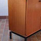 Enfilade vintage en teck années 60, deux portes pleines encadrant une vitrine centrale à portes coulissantes en verre, deux tiroirs, poignées navette métal, piétement métal laqué noir