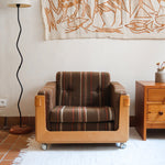 Fauteuil moderniste années 70 en bois massif clair sur roulettes avec coussins rayés bruns et terracotta.