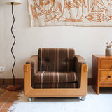 Fauteuil moderniste années 70 en bois massif clair sur roulettes avec coussins rayés bruns et terracotta.