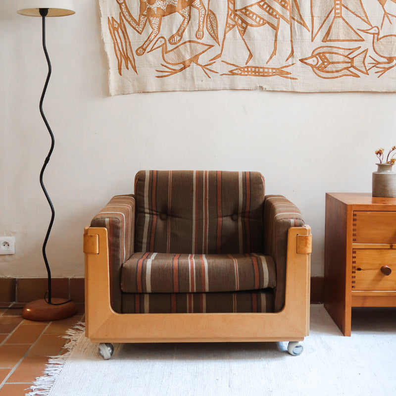 Fauteuil moderniste années 70 en bois massif clair sur roulettes avec coussins rayés bruns et terracotta.