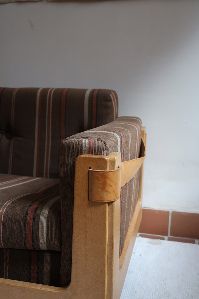 Fauteuil moderniste années 70 en bois massif clair sur roulettes avec coussins rayés bruns et terracotta.