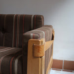 Fauteuil moderniste années 70 en bois massif clair sur roulettes avec coussins rayés bruns et terracotta.