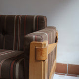 Fauteuil moderniste années 70 en bois massif clair sur roulettes avec coussins rayés bruns et terracotta.