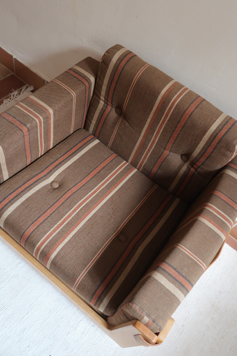 Fauteuil moderniste années 70 en bois massif clair sur roulettes avec coussins rayés bruns et terracotta.