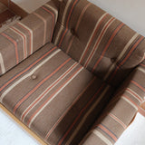 Fauteuil moderniste années 70 en bois massif clair sur roulettes avec coussins rayés bruns et terracotta.