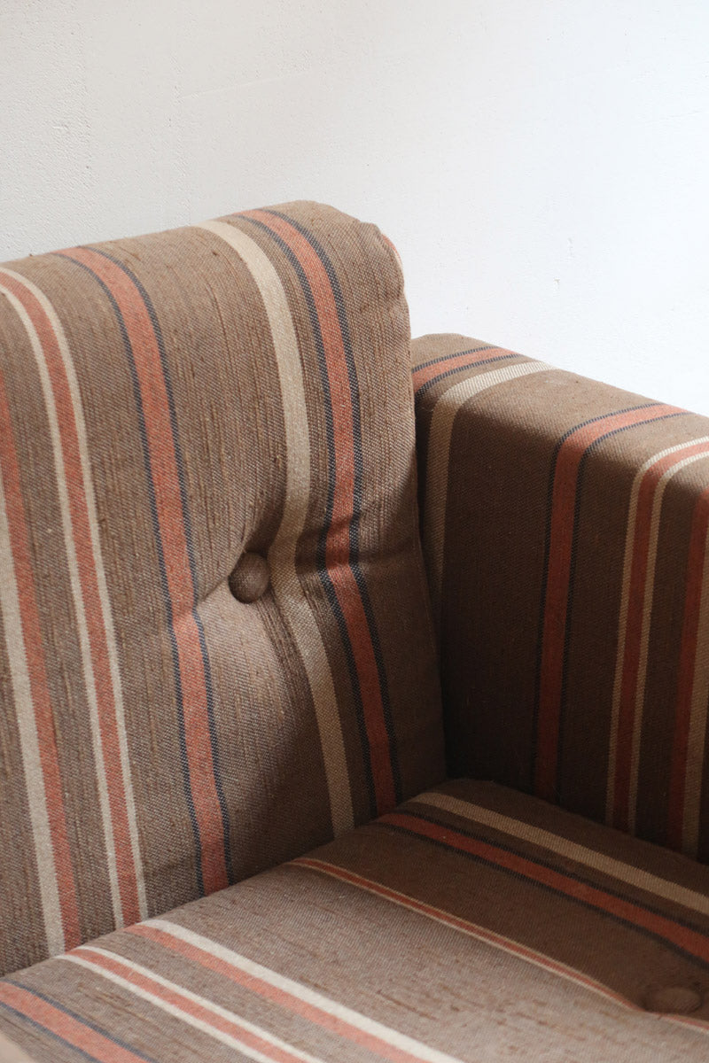 Fauteuil moderniste années 70 en bois massif clair sur roulettes avec coussins rayés bruns et terracotta.
