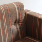 Fauteuil moderniste années 70 en bois massif clair sur roulettes avec coussins rayés bruns et terracotta.