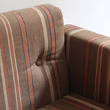 Fauteuil moderniste années 70 en bois massif clair sur roulettes avec coussins rayés bruns et terracotta.