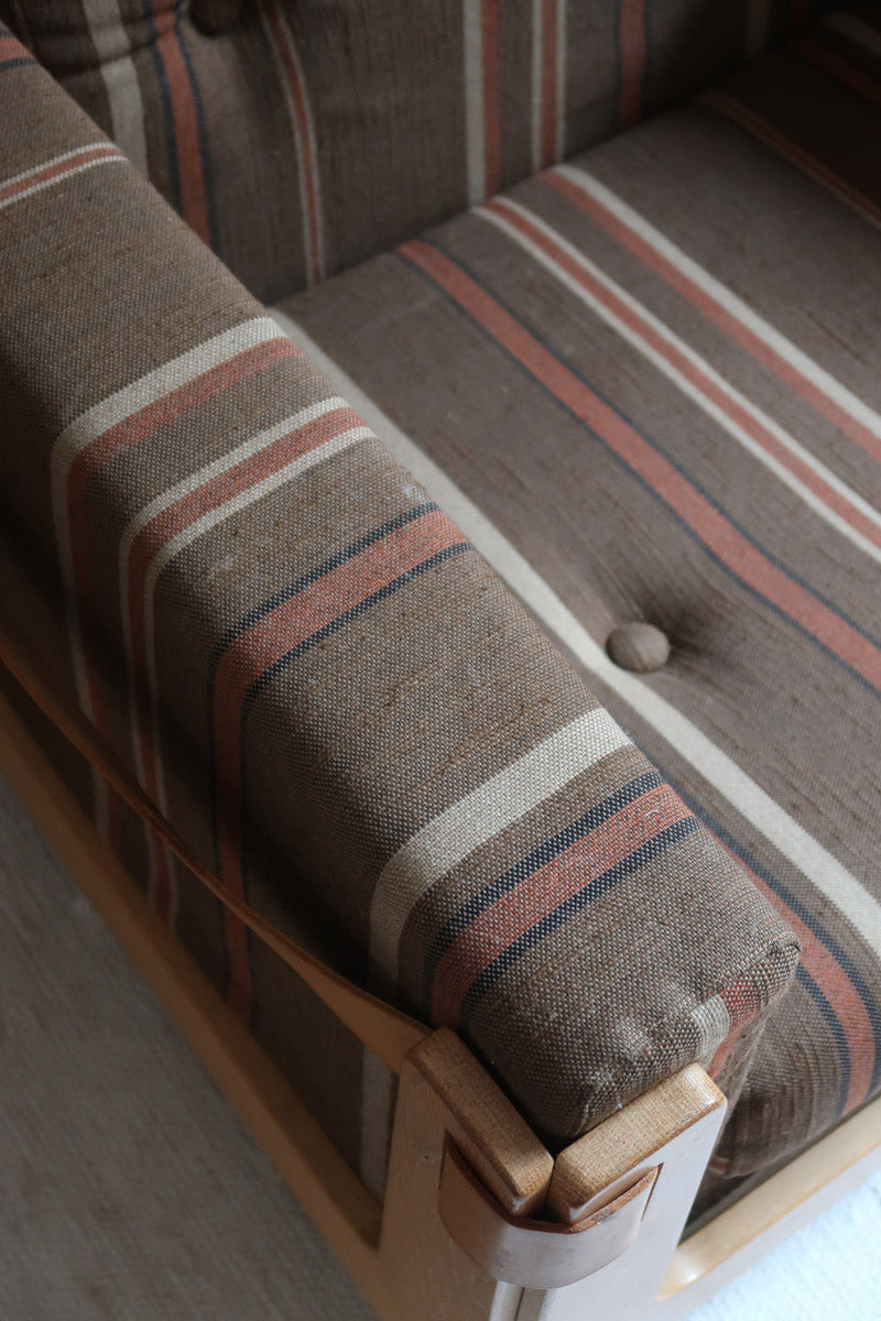 Fauteuil moderniste années 70 en bois massif clair sur roulettes avec coussins rayés bruns et terracotta.