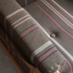 Fauteuil moderniste années 70 en bois massif clair sur roulettes avec coussins rayés bruns et terracotta.