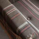 Fauteuil moderniste années 70 en bois massif clair sur roulettes avec coussins rayés bruns et terracotta.