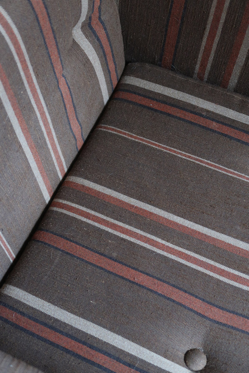 Fauteuil moderniste années 70 en bois massif clair sur roulettes avec coussins rayés bruns et terracotta.