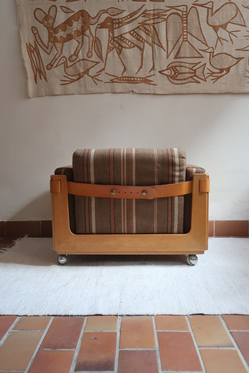 Fauteuil moderniste années 70 en bois massif clair sur roulettes avec coussins rayés bruns et terracotta.