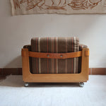 Fauteuil moderniste années 70 en bois massif clair sur roulettes avec coussins rayés bruns et terracotta.