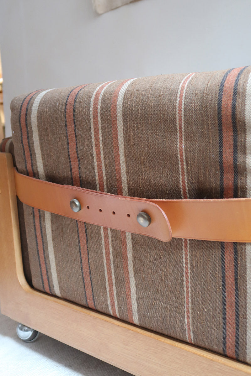 Fauteuil moderniste années 70 en bois massif clair sur roulettes avec coussins rayés bruns et terracotta.