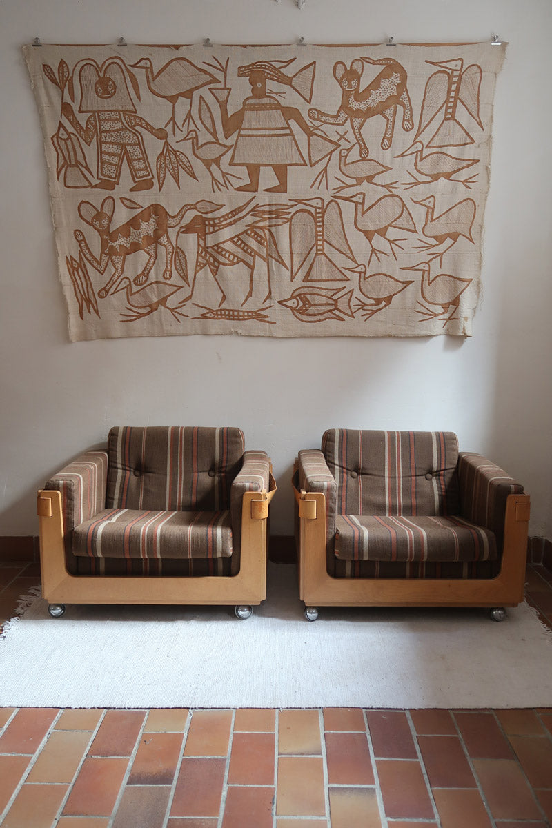 Fauteuil moderniste années 70 en bois massif clair sur roulettes avec coussins rayés bruns et terracotta.
