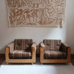 Fauteuil moderniste années 70 en bois massif clair sur roulettes avec coussins rayés bruns et terracotta.