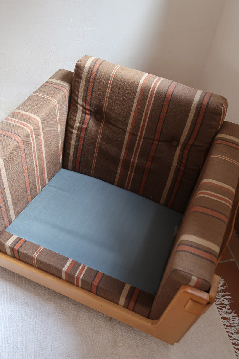 Fauteuil moderniste années 70 en bois massif clair sur roulettes avec coussins rayés bruns et terracotta.