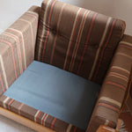 Fauteuil moderniste années 70 en bois massif clair sur roulettes avec coussins rayés bruns et terracotta.