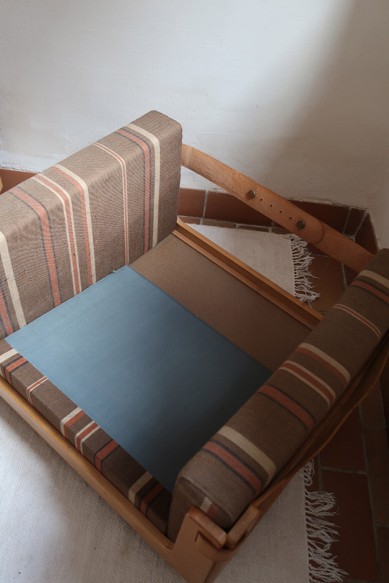 Fauteuil moderniste années 70 en bois massif clair sur roulettes avec coussins rayés bruns et terracotta.