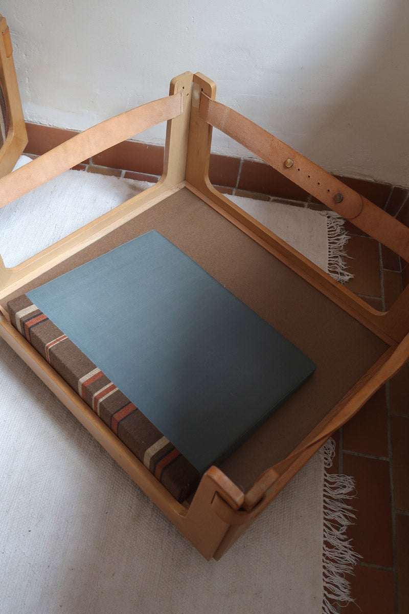 Fauteuil moderniste années 70 en bois massif clair sur roulettes avec coussins rayés bruns et terracotta.