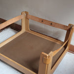 Fauteuil moderniste années 70 en bois massif clair sur roulettes avec coussins rayés bruns et terracotta.