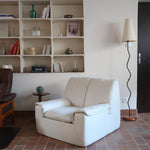 Fauteuil vintage Cinna en cuir crème années 70, étiquette d'origine cousue dans le dossier, accoudoirs et dossier en gros boudins de cuir, coussin d'assise, base pleine posée au sol sans pieds apparents