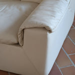 Fauteuil vintage Cinna en cuir crème années 70, étiquette d'origine cousue dans le dossier, accoudoirs et dossier en gros boudins de cuir, coussin d'assise, base pleine posée au sol sans pieds apparents
