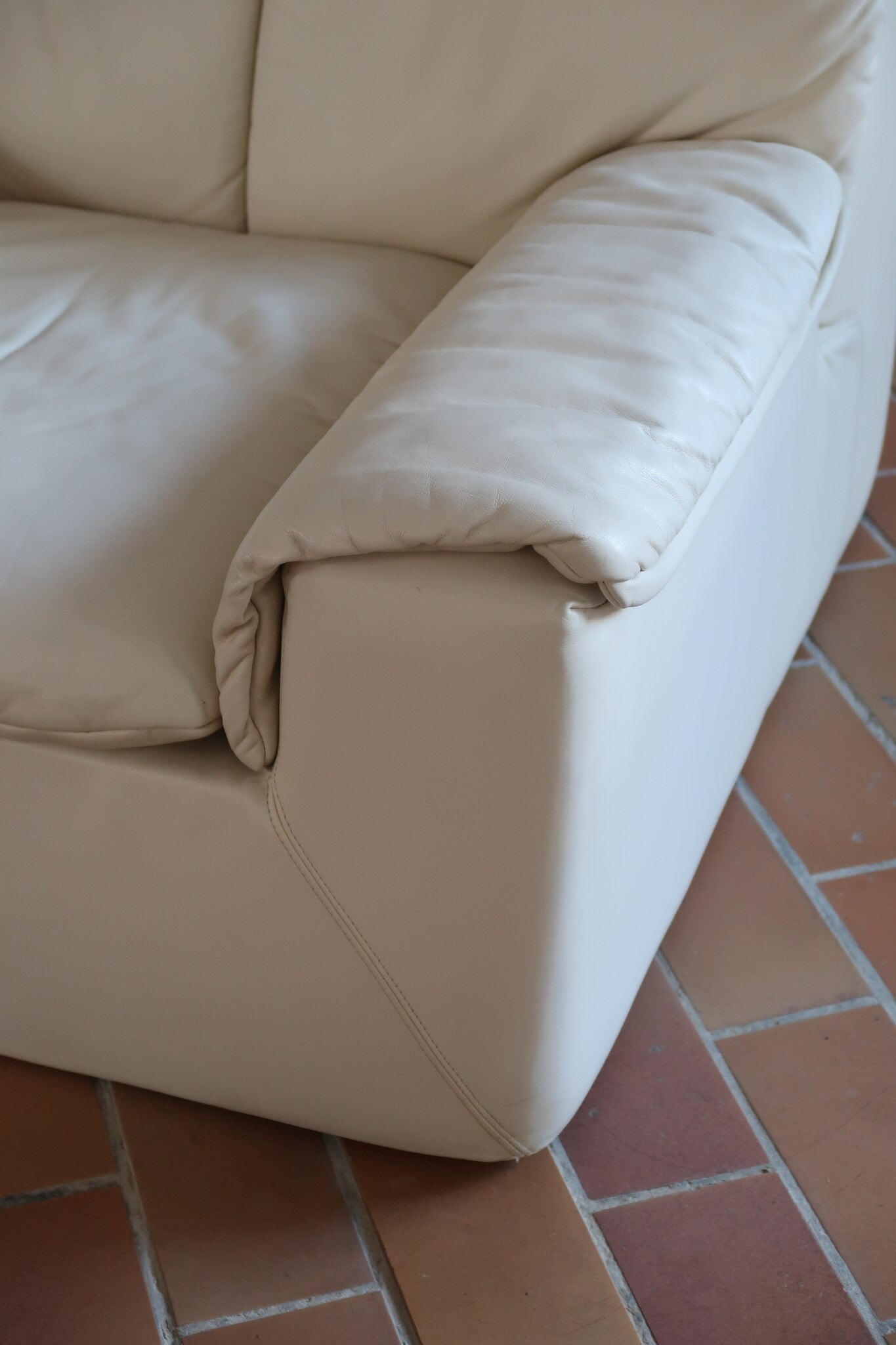 Fauteuil vintage Cinna en cuir crème années 70, étiquette d'origine cousue dans le dossier, accoudoirs et dossier en gros boudins de cuir, coussin d'assise, base pleine posée au sol sans pieds apparents
