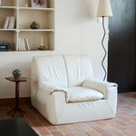 Fauteuil vintage Cinna en cuir crème années 70, étiquette d'origine cousue dans le dossier, accoudoirs et dossier en gros boudins de cuir, coussin d'assise, base pleine posée au sol sans pieds apparents