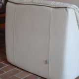 Fauteuil vintage Cinna en cuir crème années 70, étiquette d'origine cousue dans le dossier, accoudoirs et dossier en gros boudins de cuir, coussin d'assise, base pleine posée au sol sans pieds apparents