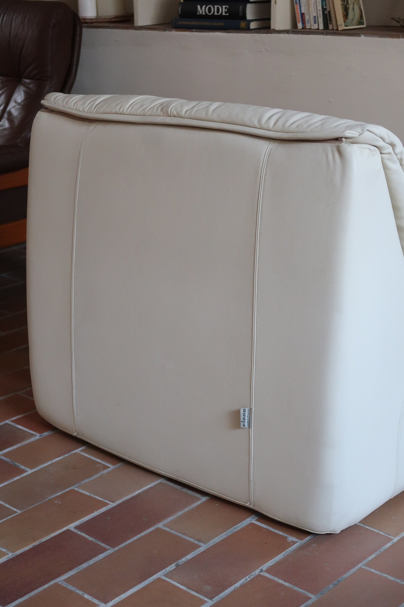 Fauteuil vintage Cinna en cuir crème années 70, étiquette d'origine cousue dans le dossier, accoudoirs et dossier en gros boudins de cuir, coussin d'assise, base pleine posée au sol sans pieds apparents
