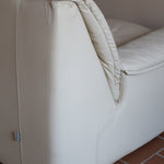 Fauteuil vintage Cinna en cuir crème années 70, étiquette d'origine cousue dans le dossier, accoudoirs et dossier en gros boudins de cuir, coussin d'assise, base pleine posée au sol sans pieds apparents