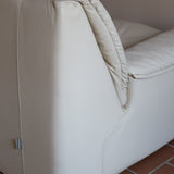 Fauteuil vintage Cinna en cuir crème années 70, étiquette d'origine cousue dans le dossier, accoudoirs et dossier en gros boudins de cuir, coussin d'assise, base pleine posée au sol sans pieds apparents