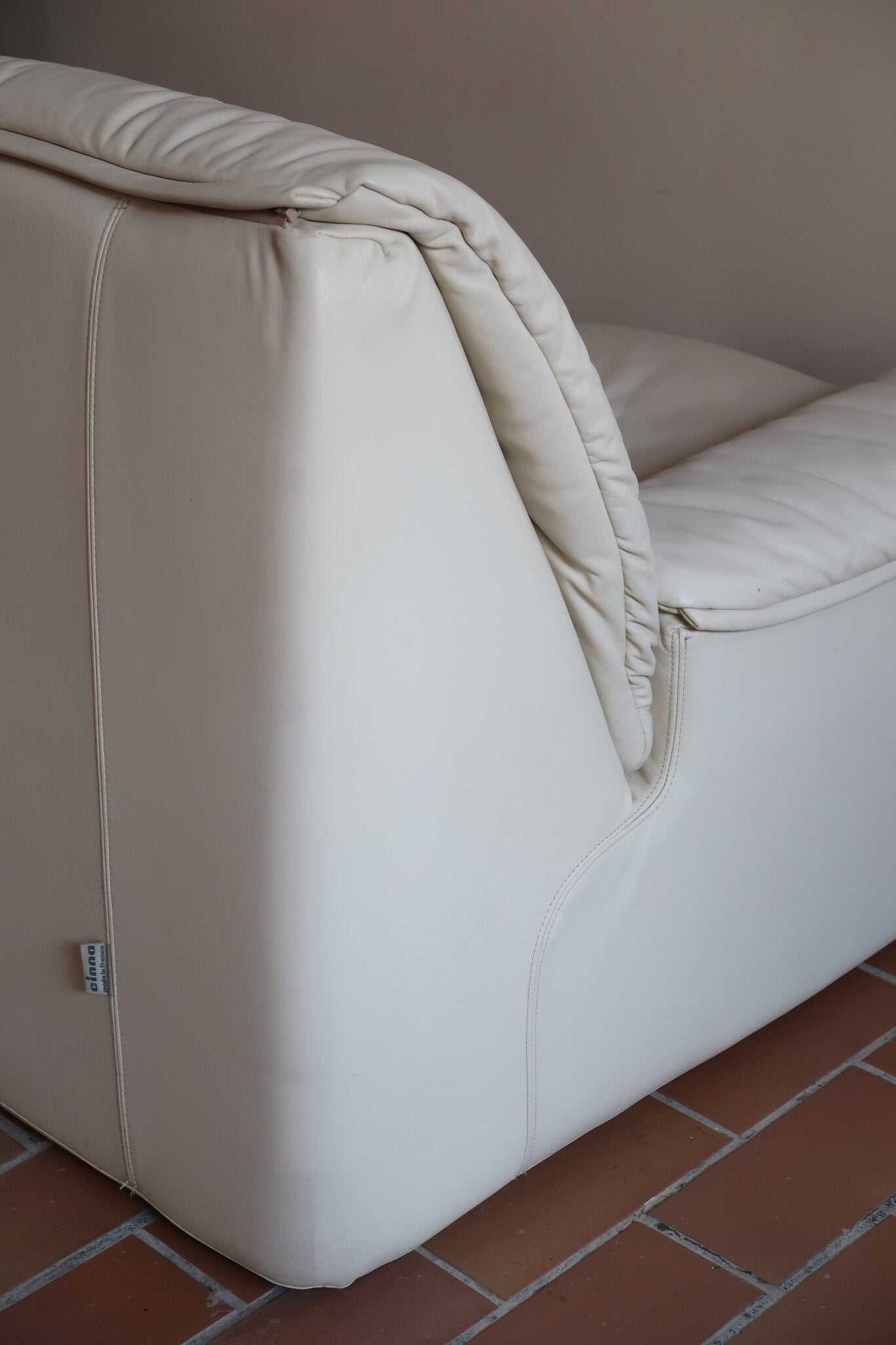Fauteuil vintage Cinna en cuir crème années 70, étiquette d'origine cousue dans le dossier, accoudoirs et dossier en gros boudins de cuir, coussin d'assise, base pleine posée au sol sans pieds apparents