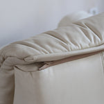 Fauteuil vintage Cinna en cuir crème années 70, étiquette d'origine cousue dans le dossier, accoudoirs et dossier en gros boudins de cuir, coussin d'assise, base pleine posée au sol sans pieds apparents