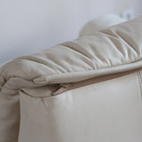 Fauteuil vintage Cinna en cuir crème années 70, étiquette d'origine cousue dans le dossier, accoudoirs et dossier en gros boudins de cuir, coussin d'assise, base pleine posée au sol sans pieds apparents