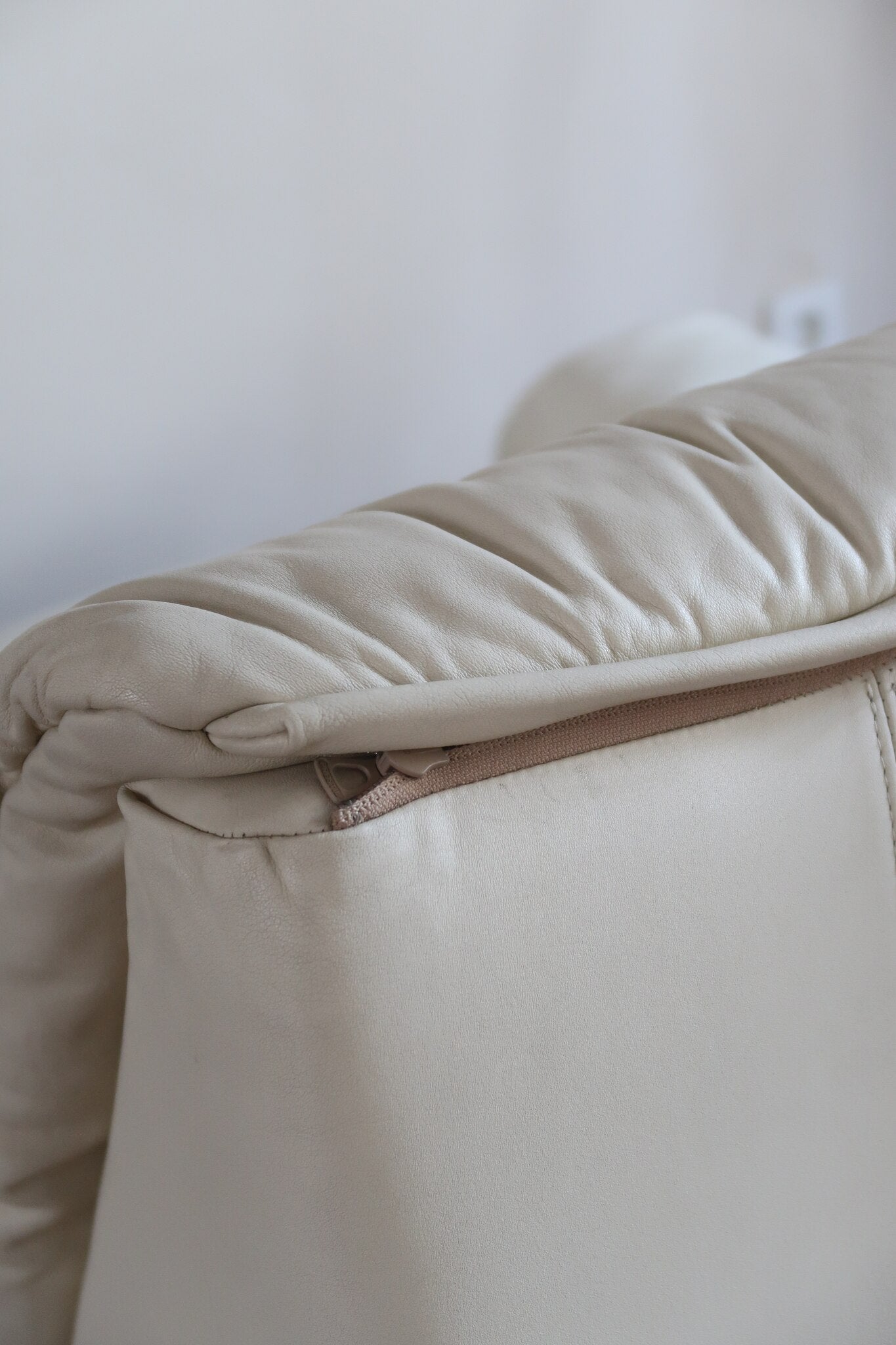 Fauteuil vintage Cinna en cuir crème années 70, étiquette d'origine cousue dans le dossier, accoudoirs et dossier en gros boudins de cuir, coussin d'assise, base pleine posée au sol sans pieds apparents