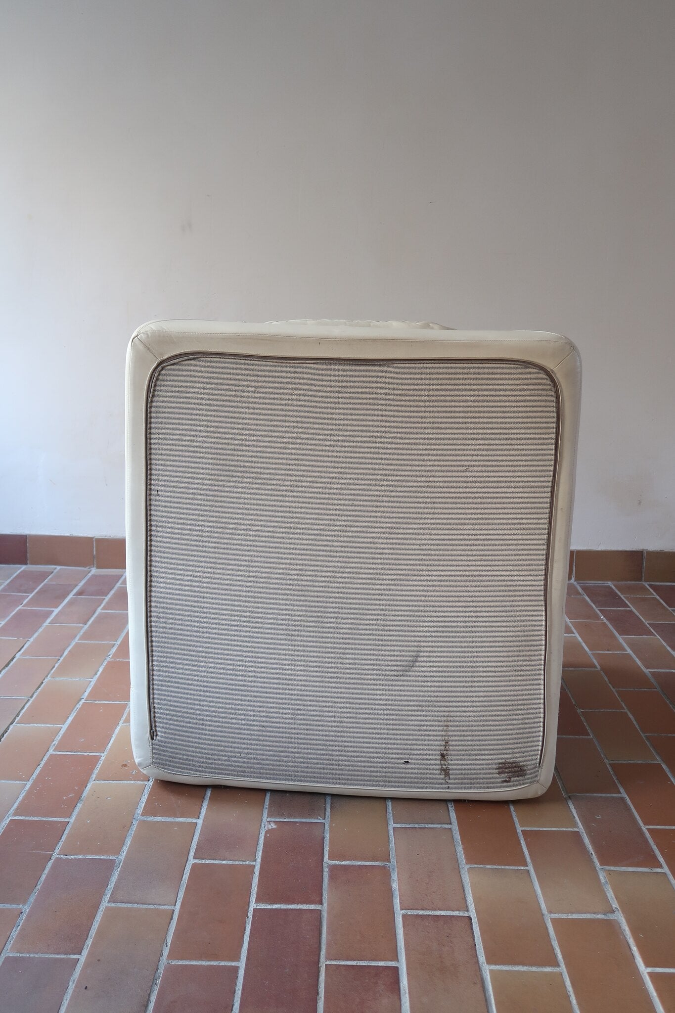 Fauteuil vintage Cinna en cuir crème années 70, étiquette d'origine cousue dans le dossier, accoudoirs et dossier en gros boudins de cuir, coussin d'assise, base pleine posée au sol sans pieds apparents