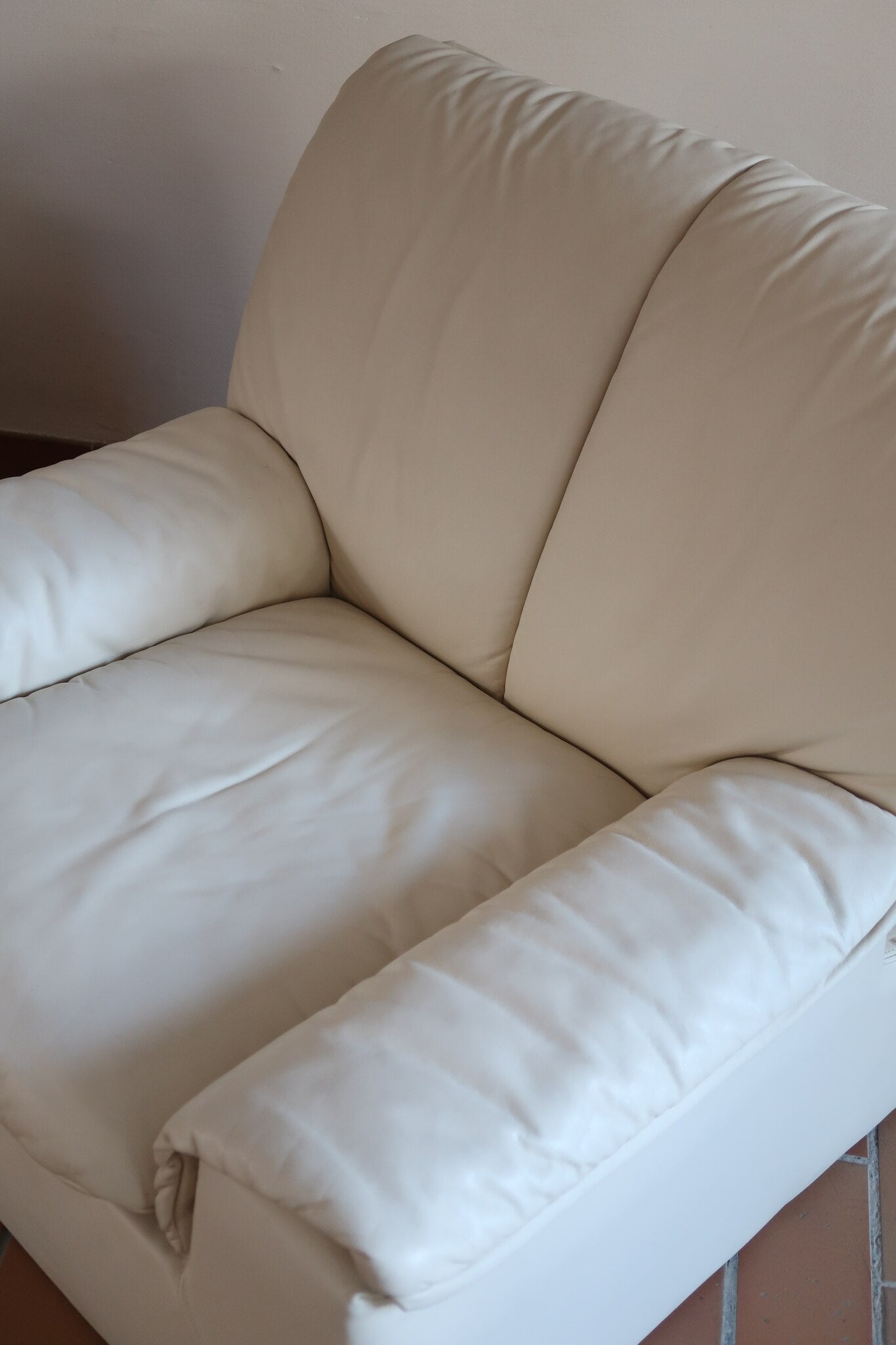 Fauteuil vintage Cinna en cuir crème années 70, étiquette d'origine cousue dans le dossier, accoudoirs et dossier en gros boudins de cuir, coussin d'assise, base pleine posée au sol sans pieds apparents
