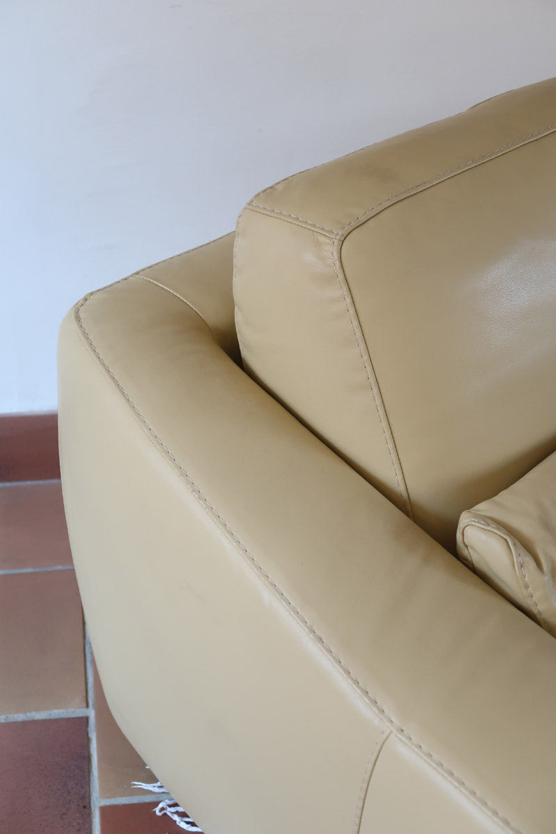 Fauteuil club vintage en cuir beige des années 80 avec accoudoirs larges et assise enveloppante.