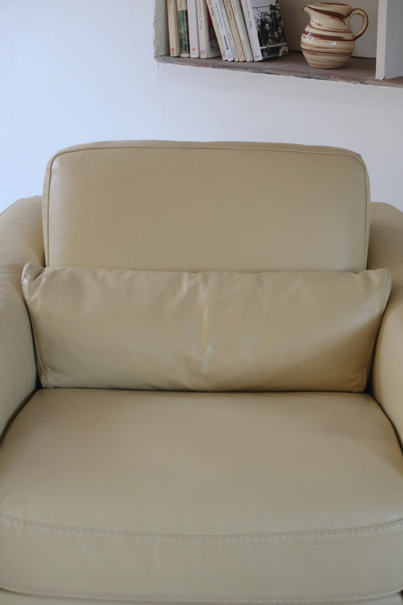 Fauteuil club vintage en cuir beige des années 80 avec accoudoirs larges et assise enveloppante.