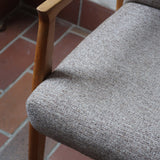 Fauteuil scandinave années 60 en bois clair avec assise retapissée tissu brun, accoudoirs galbés.