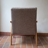 Fauteuil scandinave années 60 en bois clair avec assise retapissée tissu brun, accoudoirs galbés.
