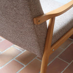 Fauteuil scandinave années 60 en bois clair avec assise retapissée tissu brun, accoudoirs galbés.