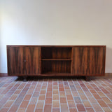 Grande enfilade vintage en palissandre de 240 cm, placage au fil en miroir, deux caissons fermant à clé de part et d'autre d'une niche centrale ouverte, tablettes intérieures en bois clair, reposant sur deux pieds pleins posés en retrait