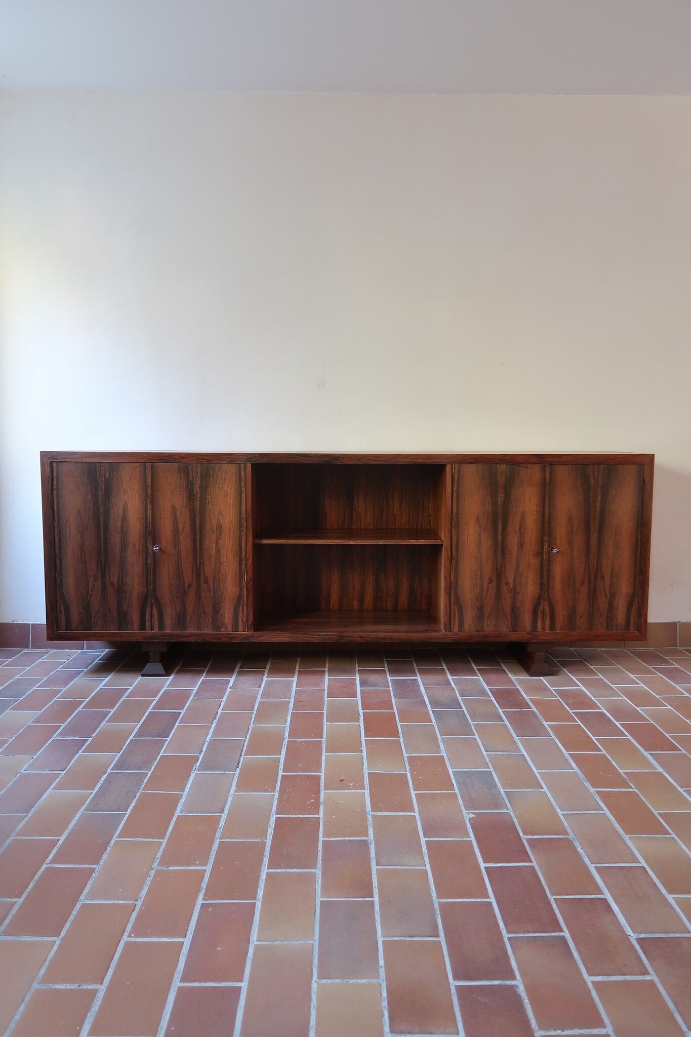 Grande enfilade vintage en palissandre de 240 cm, placage au fil en miroir, deux caissons fermant à clé de part et d'autre d'une niche centrale ouverte, tablettes intérieures en bois clair, reposant sur deux pieds pleins posés en retrait
